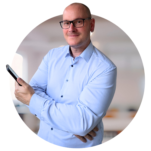 Martin Scholz, zertifizierter Sachverständiger und Gutachter für Online-Marketing in Erfurt. Freundlich lächelnder Mann mit Brille und hellblauem Hemd, ein Smartphone in der Hand, als Porträt im Kreis-Ausschnitt.